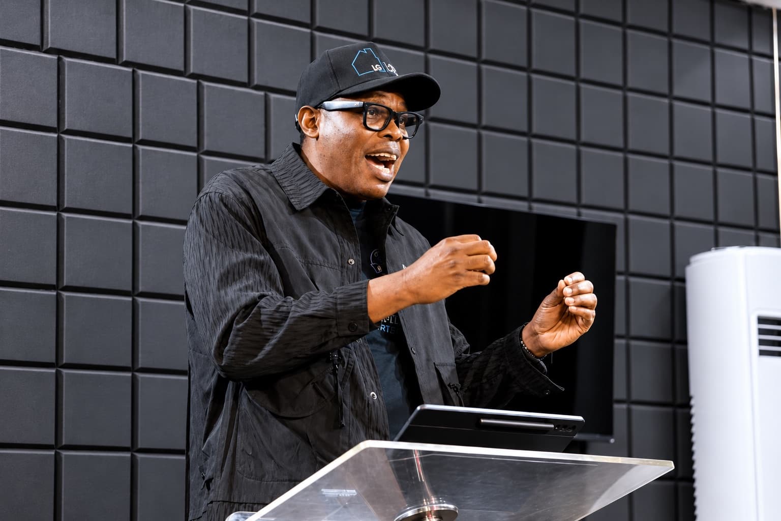 Wole Abraham Martins speaking from a lectern, hands raised mid-sentence